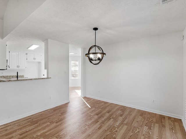 unfurnished dining area featuring a chandelier, baseboards, a textured ceiling, and light wood finished floors