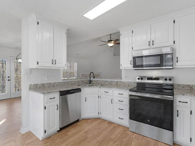 kitchen with white cabinets, light stone countertops, stainless steel appliances, light wood-style floors, and a sink