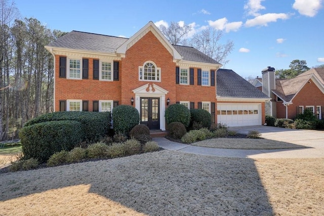 colonial house with concrete driveway, french doors, an attached garage, and brick siding