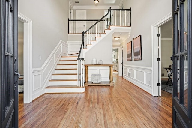 entrance foyer with a decorative wall, a towering ceiling, ornamental molding, wood finished floors, and stairs