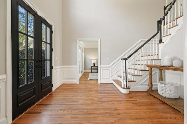 foyer featuring light wood-style floors, french doors, a wainscoted wall, and stairway