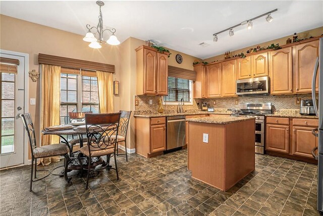 kitchen with stainless steel appliances, light stone counters, a wealth of natural light, hanging light fixtures, and a kitchen island