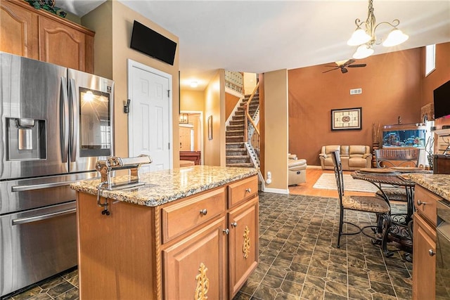 kitchen with a kitchen island, stainless steel fridge with ice dispenser, pendant lighting, light stone countertops, and ceiling fan with notable chandelier