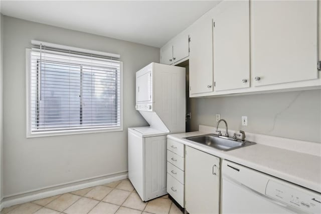 laundry area with light tile patterned floors, cabinet space, baseboards, stacked washer / dryer, and a sink