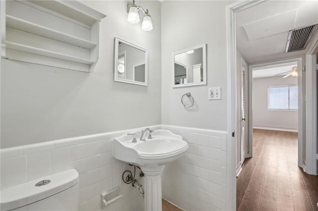 bathroom featuring a wainscoted wall, toilet, visible vents, and tile walls