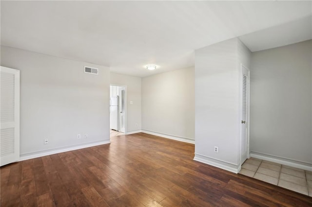 spare room with hardwood / wood-style floors, visible vents, and baseboards