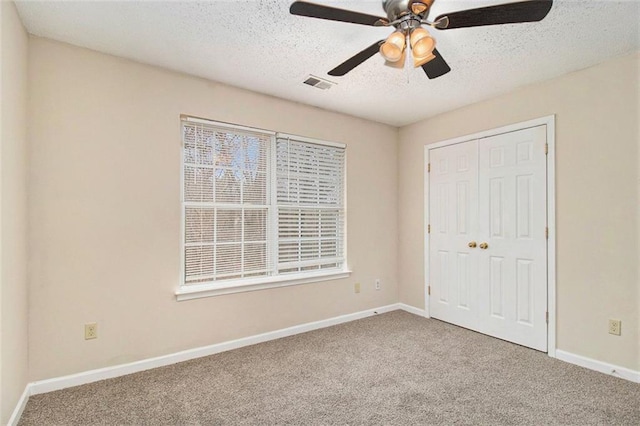 unfurnished bedroom with a textured ceiling, carpet floors, visible vents, baseboards, and a closet