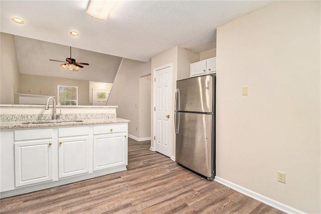 kitchen featuring baseboards, wood finished floors, freestanding refrigerator, white cabinetry, and a sink