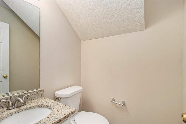 bathroom with vaulted ceiling, a textured ceiling, toilet, and vanity