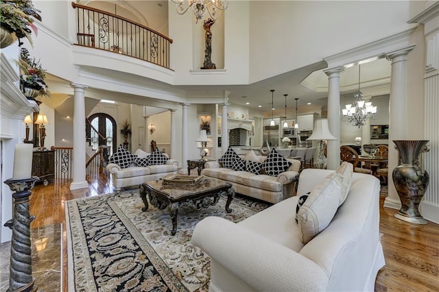 living area featuring decorative columns, wood finished floors, a high ceiling, and a notable chandelier