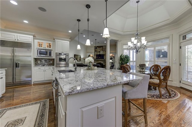kitchen featuring dark wood finished floors, ornate columns, built in appliances, and a sink