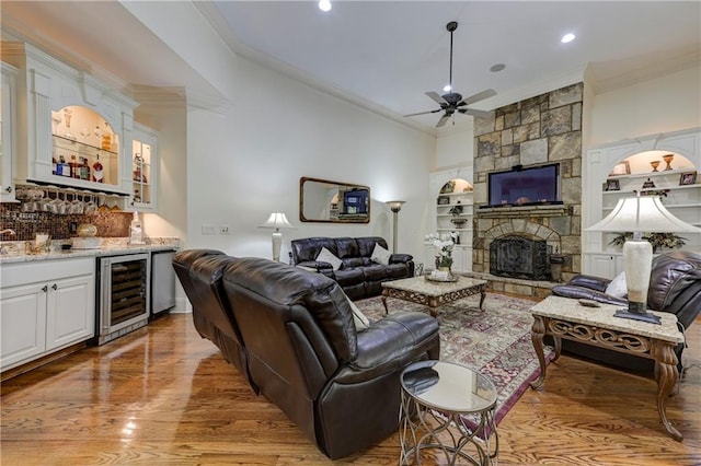 living room with light wood-style floors, ceiling fan, crown molding, indoor wet bar, and beverage cooler