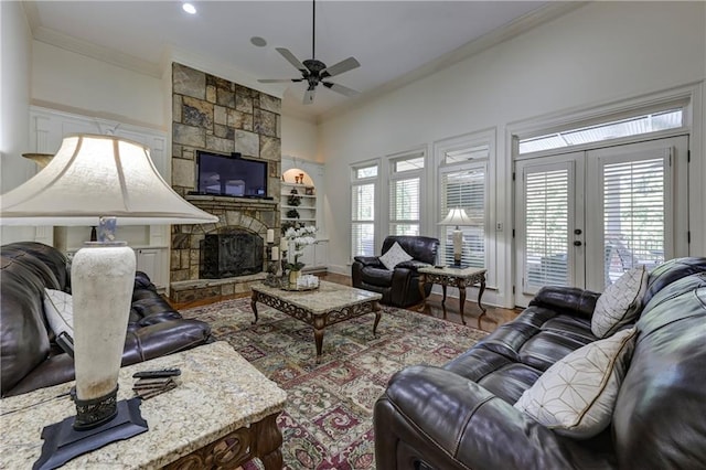 living area featuring crown molding, wood finished floors, a stone fireplace, ceiling fan, and built in features
