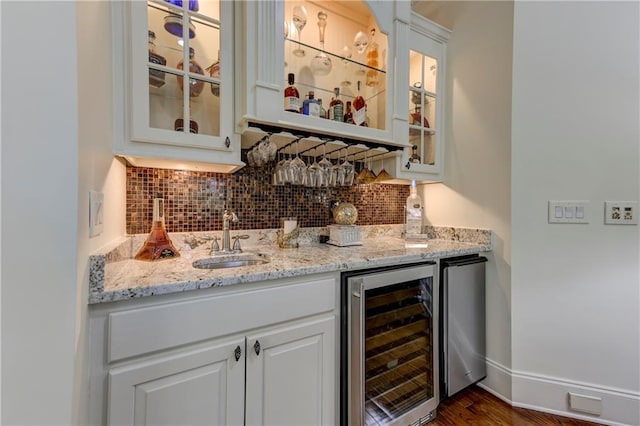 bar featuring a sink, baseboards, backsplash, indoor wet bar, and beverage cooler