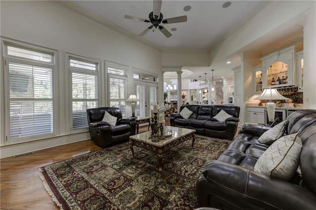 living area featuring a ceiling fan, crown molding, wood finished floors, visible vents, and decorative columns