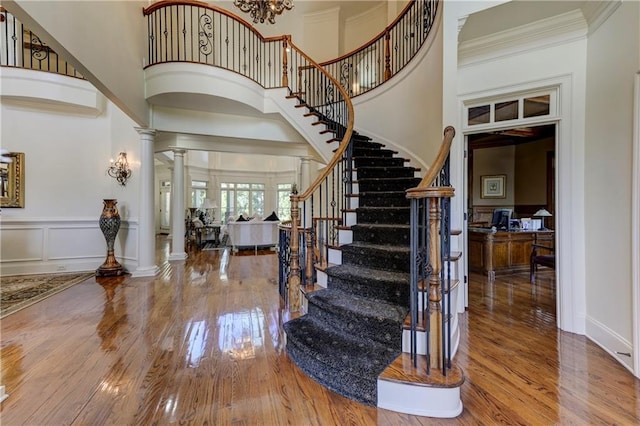 foyer featuring a towering ceiling, wood finished floors, stairs, and ornate columns