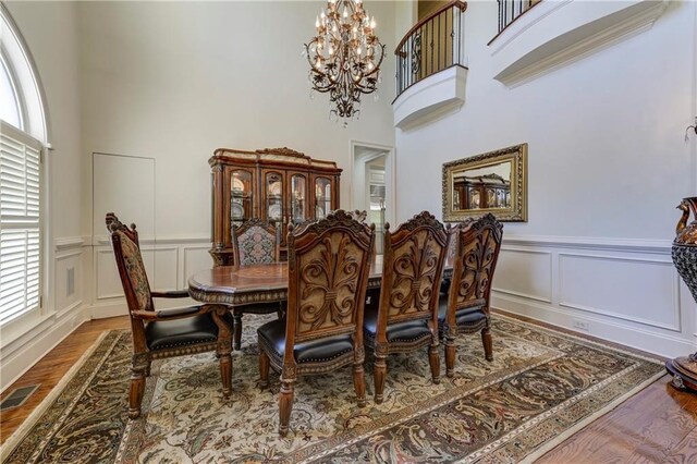 dining space with wood finished floors, visible vents, a high ceiling, and a decorative wall