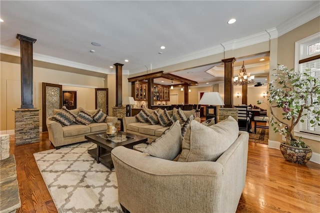 living area featuring wood finished floors, crown molding, and decorative columns