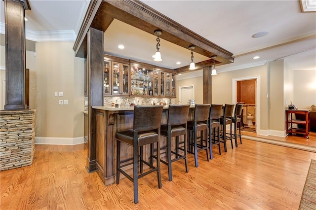 bar with light wood-type flooring, crown molding, baseboards, and indoor wet bar