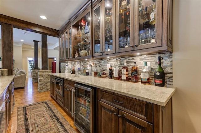 bar featuring light wood finished floors, beverage cooler, backsplash, and wet bar