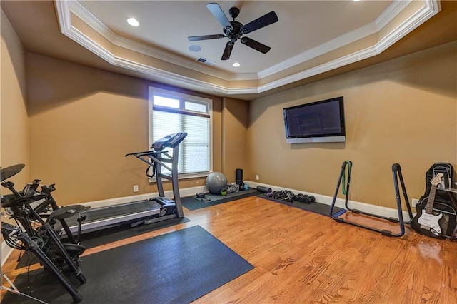 exercise area with wood finished floors, a tray ceiling, and crown molding