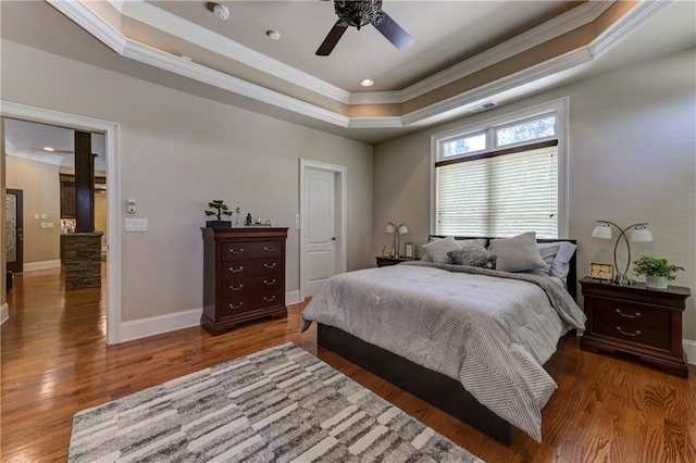 bedroom featuring a tray ceiling, wood finished floors, visible vents, crown molding, and baseboards