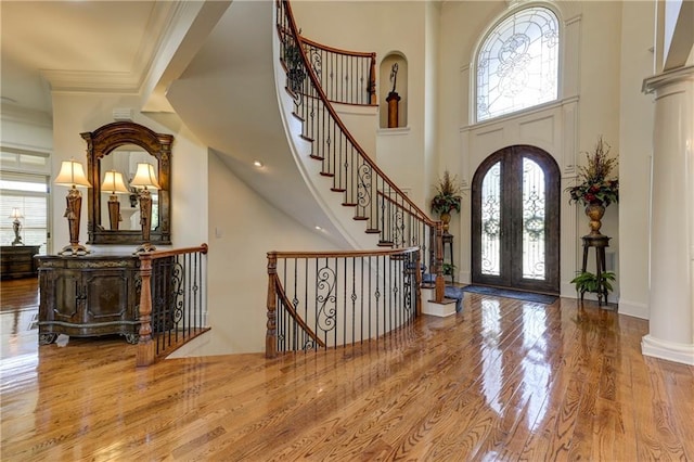 entryway featuring stairway, a towering ceiling, wood finished floors, ornamental molding, and french doors
