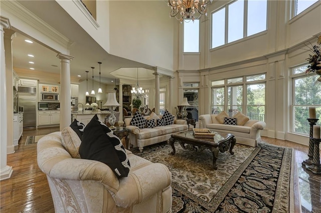 living area with a high ceiling, ornate columns, a notable chandelier, and a healthy amount of sunlight