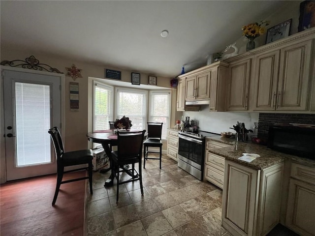 kitchen featuring stainless steel electric range oven, dark stone countertops, cream cabinetry, and wood-type flooring