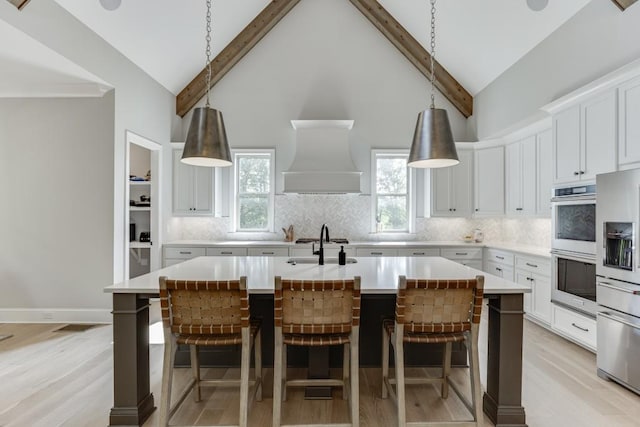 4781 Falling Brook Dr, Flowery Branch, GA 30542 - kitchen with appliances with stainless steel finishes, a center island with sink, tasteful backsplash, premium range hood, and beamed ceiling