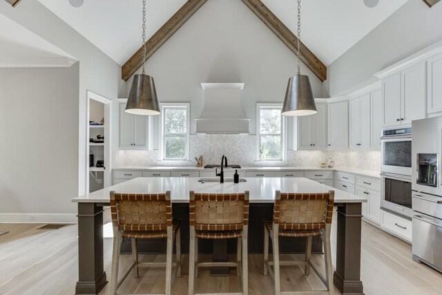 4781 Falling Brook Dr, Flowery Branch, GA 30542 - kitchen with appliances with stainless steel finishes, a center island with sink, tasteful backsplash, premium range hood, and beamed ceiling
