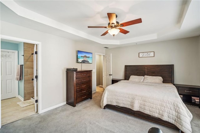 carpeted bedroom featuring ceiling fan, ensuite bath, and a tray ceiling