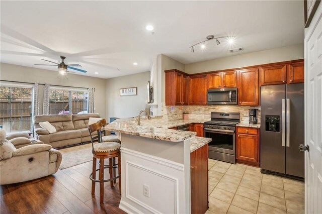 kitchen featuring kitchen peninsula, appliances with stainless steel finishes, a kitchen bar, light stone countertops, and light hardwood / wood-style flooring