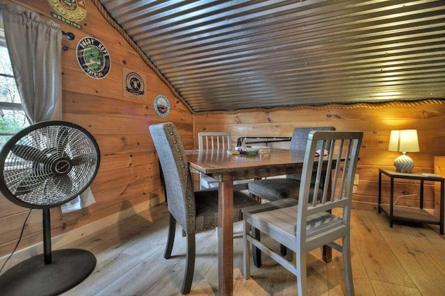 dining space featuring wooden walls, lofted ceiling, and light hardwood / wood-style flooring