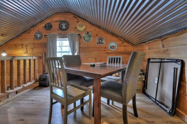 dining room with wood-type flooring, wooden walls, and vaulted ceiling