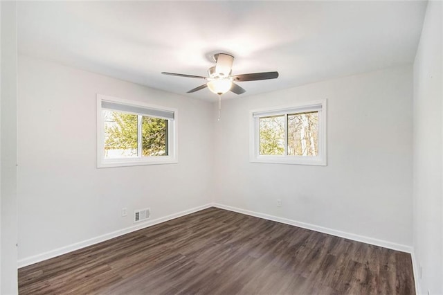 spare room featuring dark wood-type flooring, a healthy amount of sunlight, visible vents, and baseboards