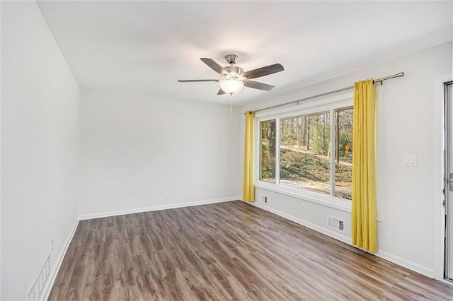 empty room with wood finished floors, a ceiling fan, visible vents, and baseboards