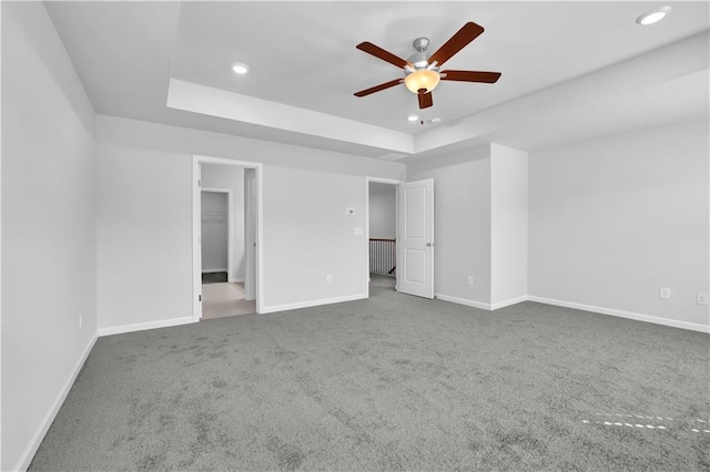 unfurnished bedroom featuring carpet, a spacious closet, ceiling fan, and a tray ceiling