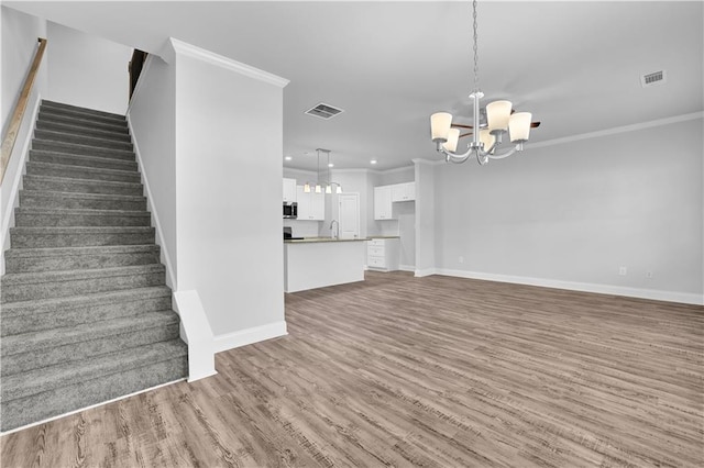 unfurnished living room featuring an inviting chandelier, dark hardwood / wood-style flooring, sink, and crown molding