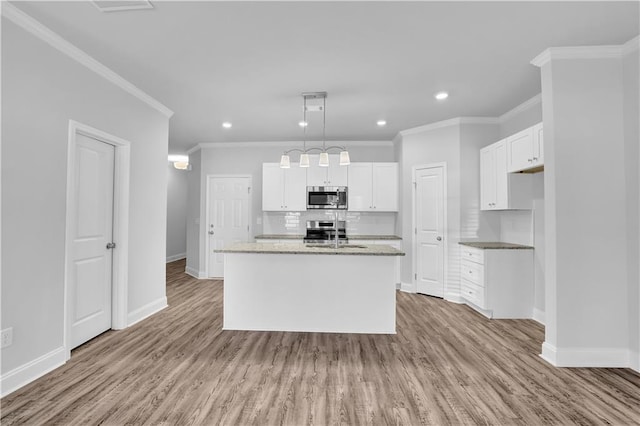 kitchen with appliances with stainless steel finishes, decorative light fixtures, white cabinetry, an island with sink, and backsplash