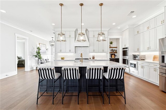 kitchen with decorative light fixtures, white cabinetry, and a center island with sink