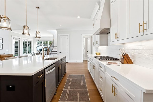 kitchen featuring a kitchen island with sink, white cabinets, pendant lighting, stainless steel appliances, and wall chimney exhaust hood