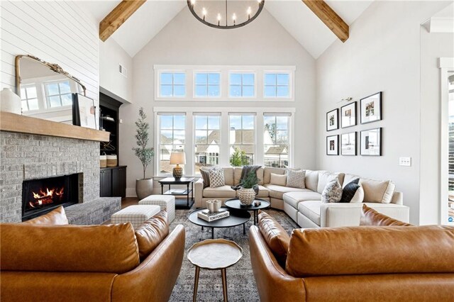 living room with an inviting chandelier, beam ceiling, high vaulted ceiling, and a brick fireplace