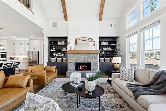 living room with a high ceiling, beamed ceiling, a brick fireplace, and a wealth of natural light