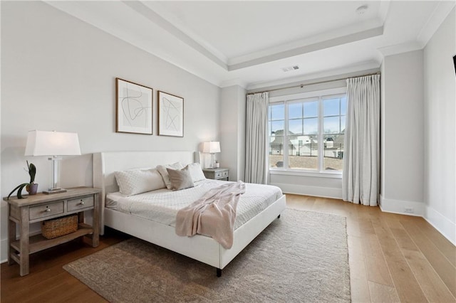 bedroom with hardwood / wood-style flooring, crown molding, and a raised ceiling