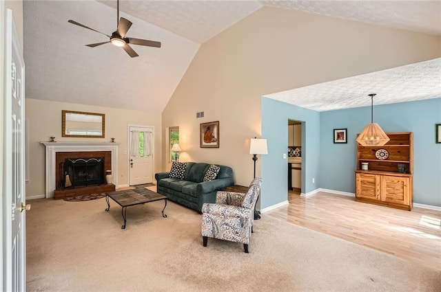 carpeted living room featuring high vaulted ceiling, a ceiling fan, baseboards, and a fireplace with raised hearth