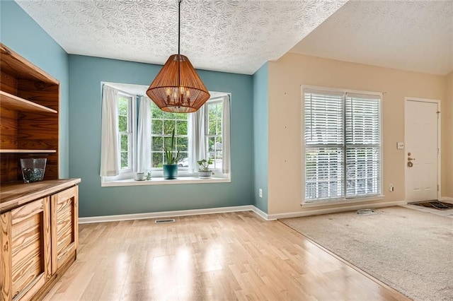 unfurnished dining area with wood finished floors, a textured ceiling, baseboards, and a chandelier