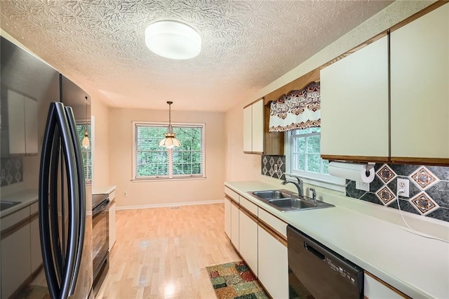 kitchen with black appliances, a sink, light wood-style floors, decorative backsplash, and light countertops