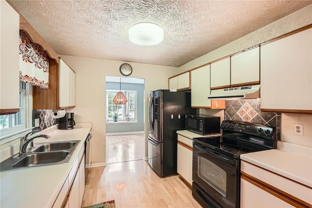 kitchen with black appliances, under cabinet range hood, a sink, light countertops, and a textured ceiling
