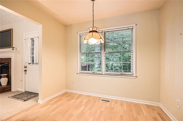 unfurnished dining area with light wood-style floors, baseboards, and a fireplace with raised hearth